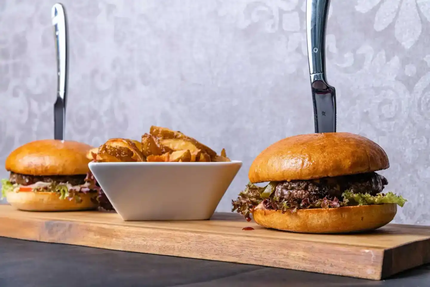 Zwei appetitliche Burger und goldene Kartoffelpommes auf Holzbrett – Foodfotografie Wien