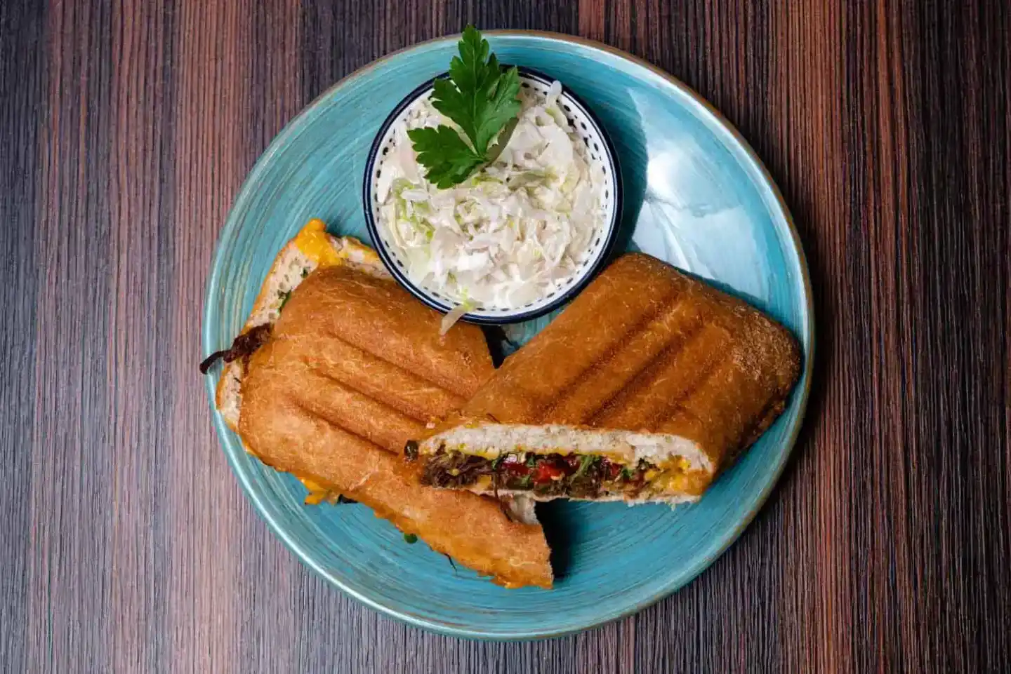 Gegrillte Sandwiches mit Fleischfüllung und Dip-Sauce auf blauem Teller – Foodfotografie Wien