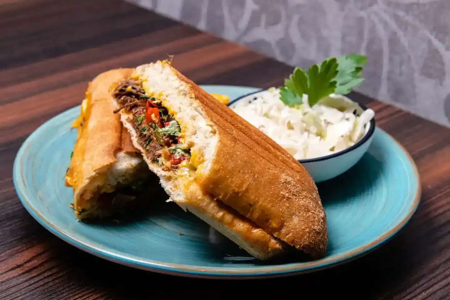 Gourmet Sandwich mit Rinderfleisch, Käse und frischen Kräutern auf blauem Teller, serviert mit Coleslaw - Food Fotografie Wie