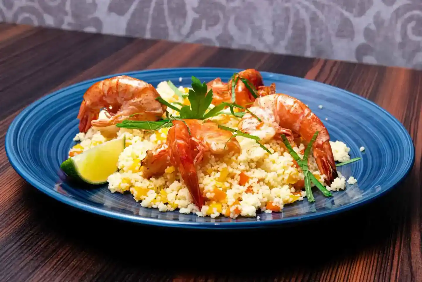 Köstliches Garnelen-Couscous Gericht mit frischen Kräutern und Limettenkeil auf blauem Teller - Food Fotografie Wien