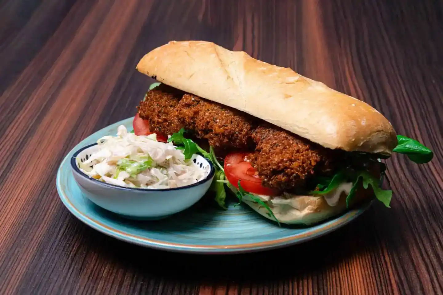 Knuspriges Schnitzel-Sandwich mit Tomaten und Rucola auf hellblauem Teller, serviert mit Krautsalat von unserem Food Fotograf
