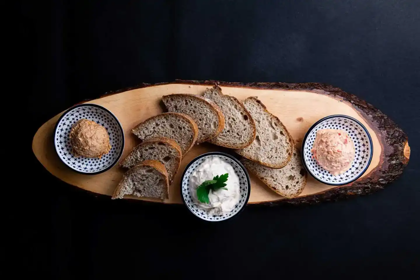 Rustikale Brotzuschnitte mit drei Dips auf Holzboard - professionelle Foodfotografie Wien