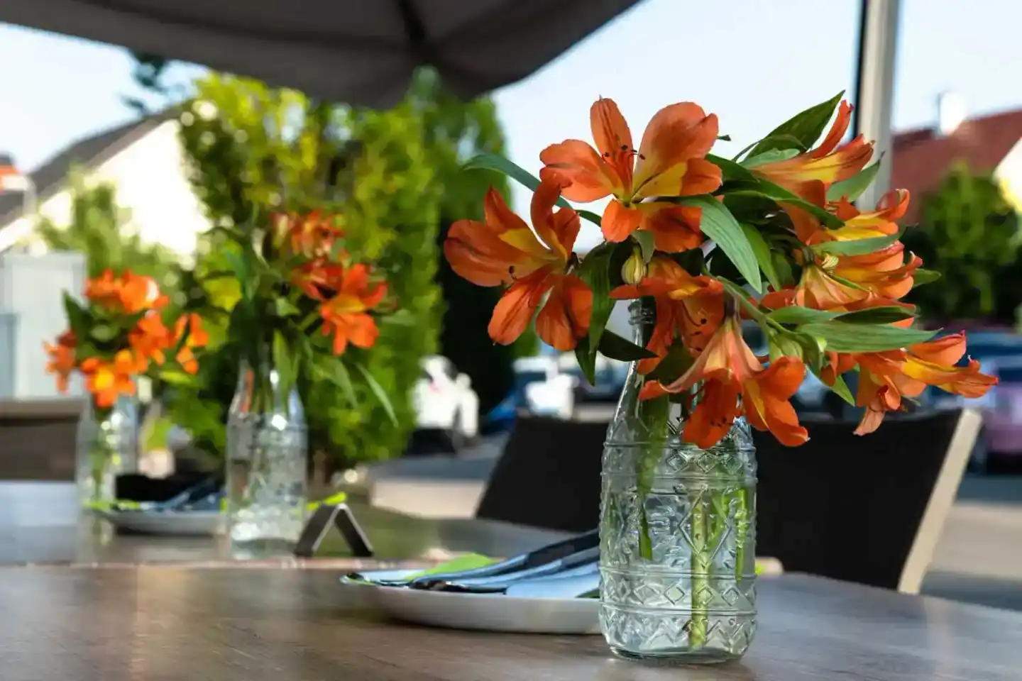 Elegante Tischdekoraration mit orange-roten Amaryllis-Blüten in Glasvase, professionelle Restaurant Fotografie Wien unter Son