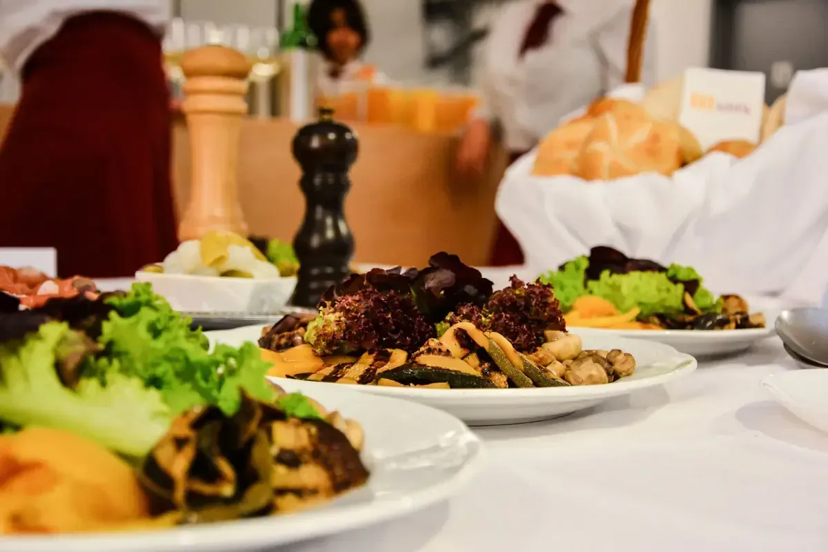 Elegante Restaurantaufnahme mit kunstvoll angerichteten Tellern: Gegrilltes Fleisch mit Gemüse und Salatgarnitur auf weißem P