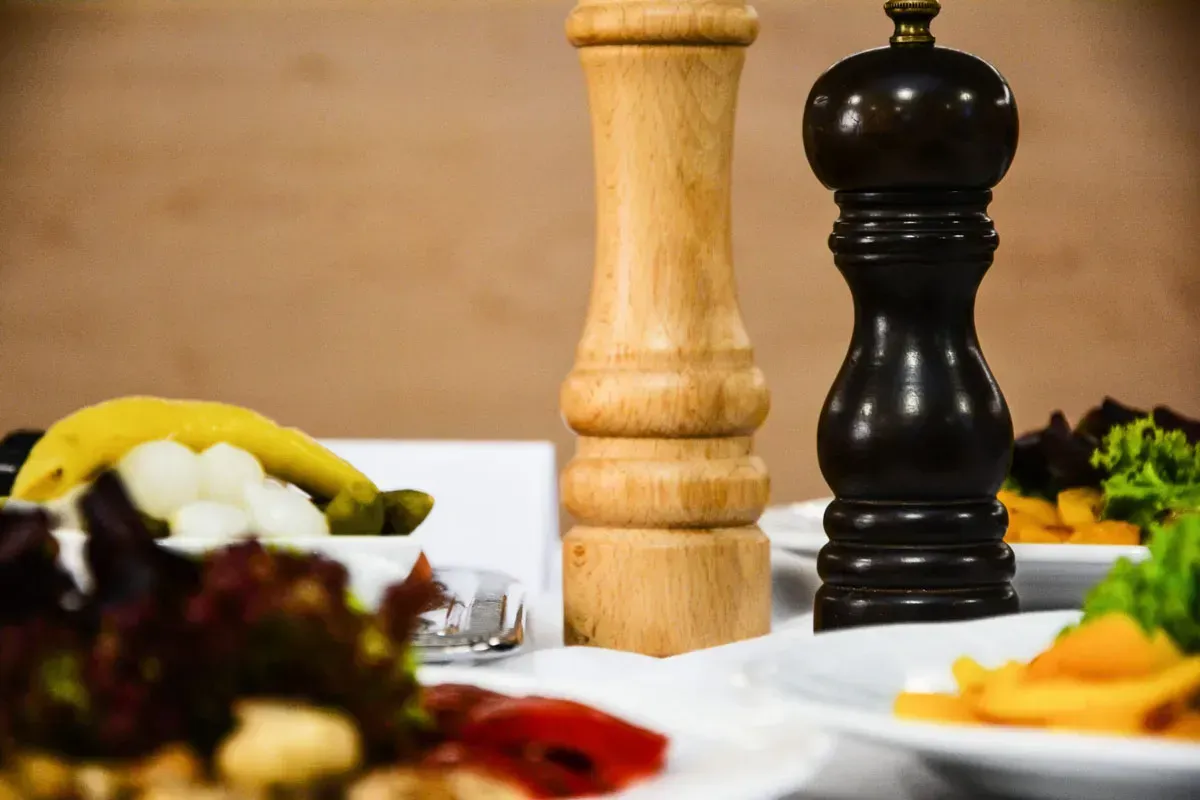 Elegante Tischeindeckung mit Holz-Pfeffermühle, natürlichem Salzstreuer und frischen Zutaten – professionelle Foodfotografie