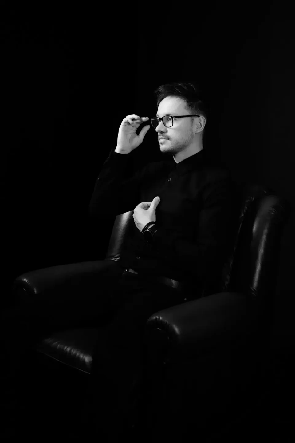 Mann mit Brille in schwarzem Hemd sitzt nachdenklich auf Ledersofa, professionelles Portrait von Portraitfotograf Wien