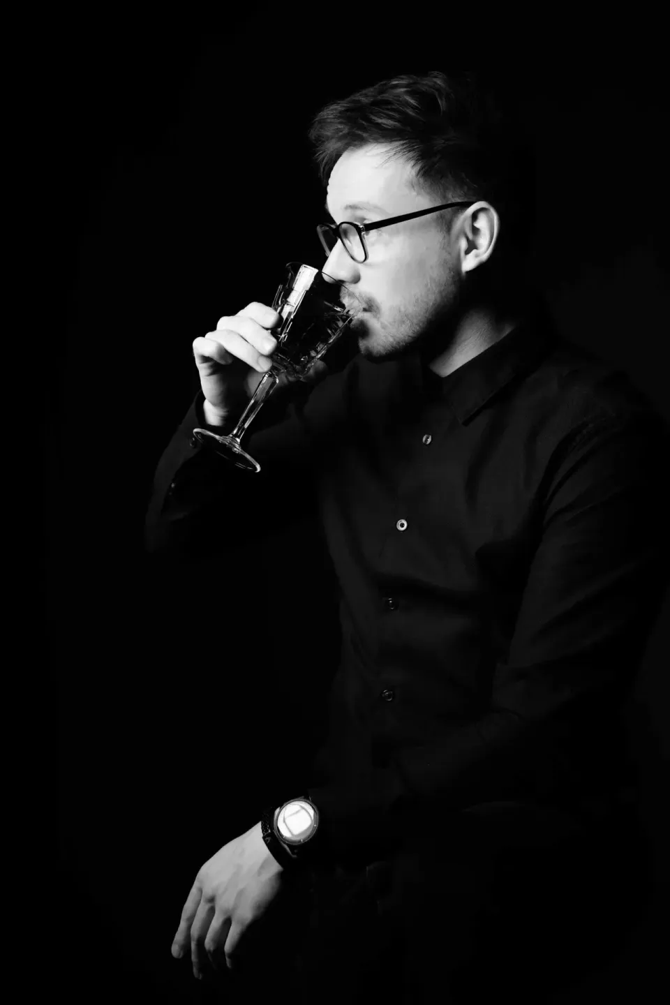 Porträtfoto eines Mannes mit Brille in schwarzem Hemd, der aus einem Glas trinkt – professionelles Portrait von Portraitfotog