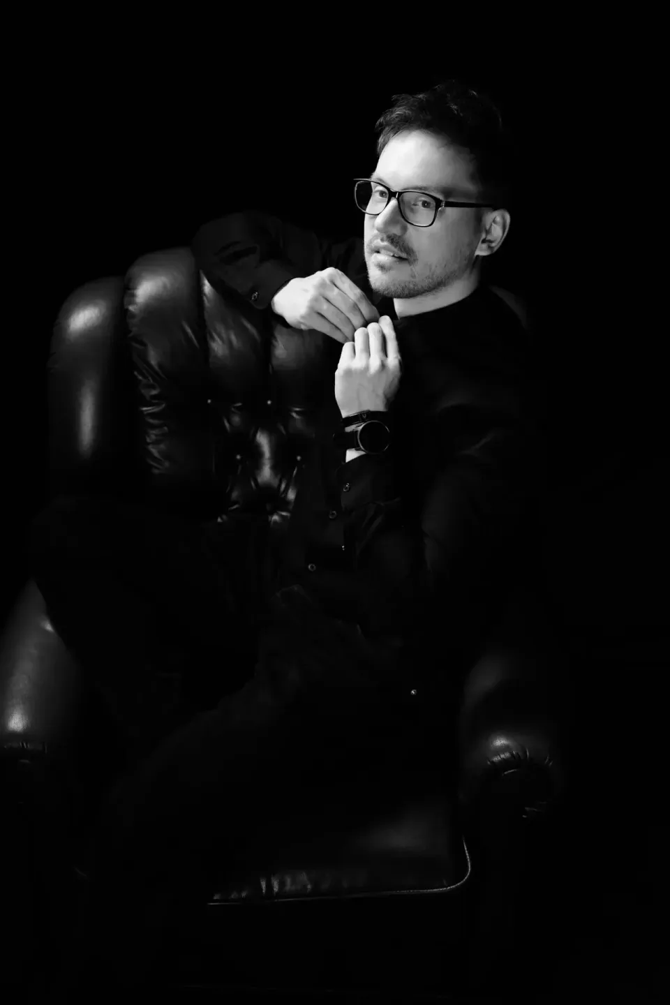 Mann mit Brille in schwarzer Lederjacke sitzt nachdenklich auf Stuhl – professionelles Portrait Wien