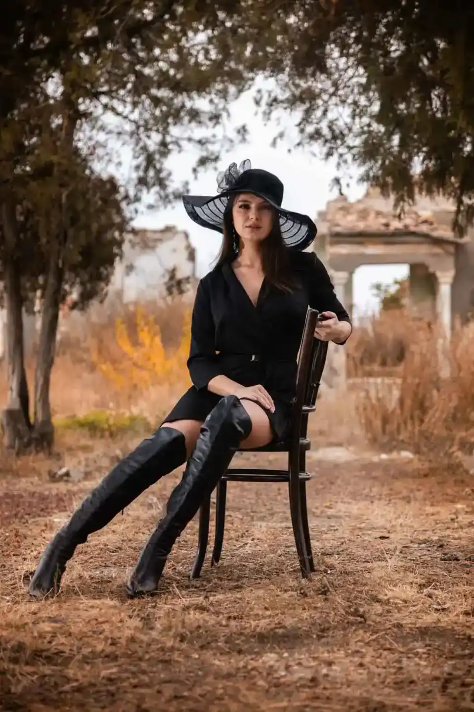 Elegantes Porträt einer Frau im schwarzen Blazer und breiter Hut, sitzend unter Bäumen - professionelle Portraitfotografie Wi