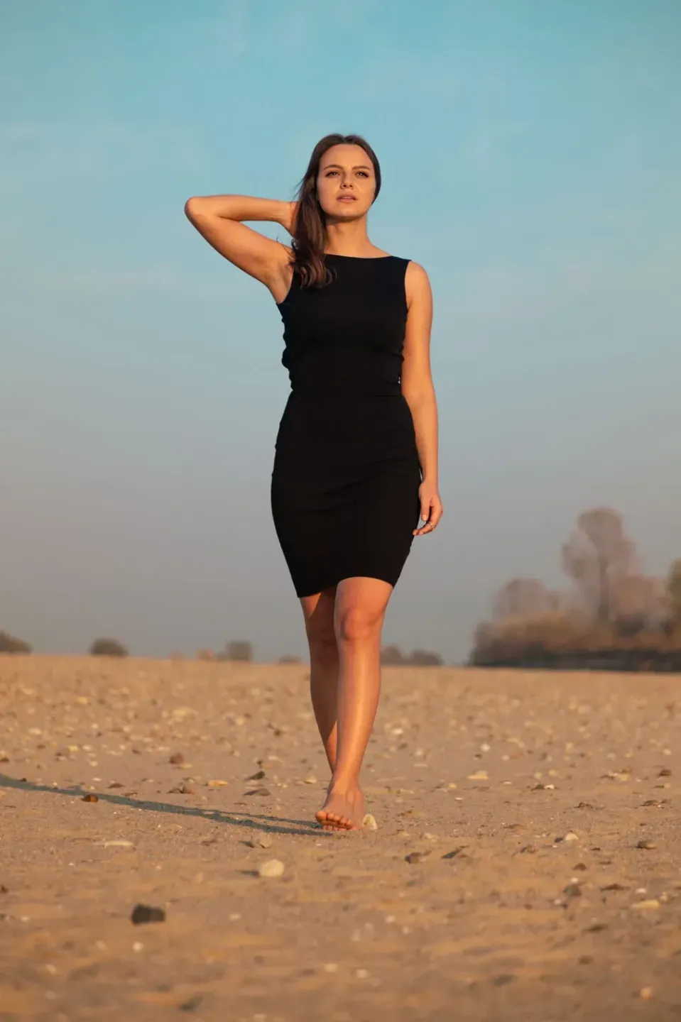 Frau in schwarzem Kleid steht barfuß in einer Sandlandschaft, Portrait Wien vor blauem Himmel