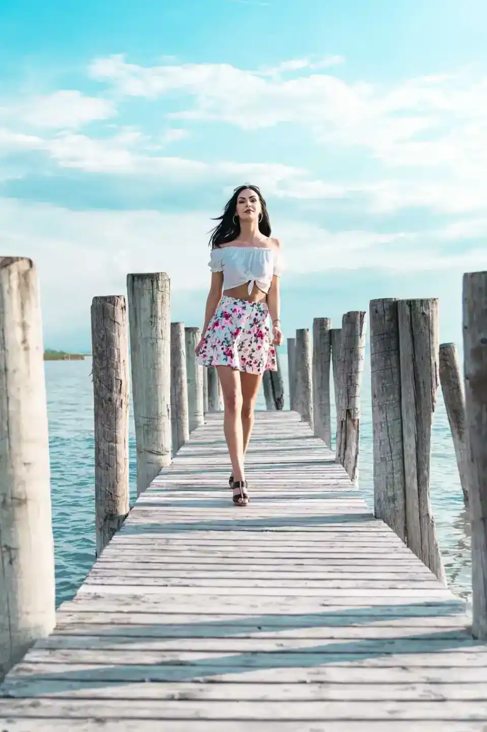 Junge Frau in weißem Crop-Top und Blumenmuster-Rock auf Holzsteg am Wasser, Portrait Wien