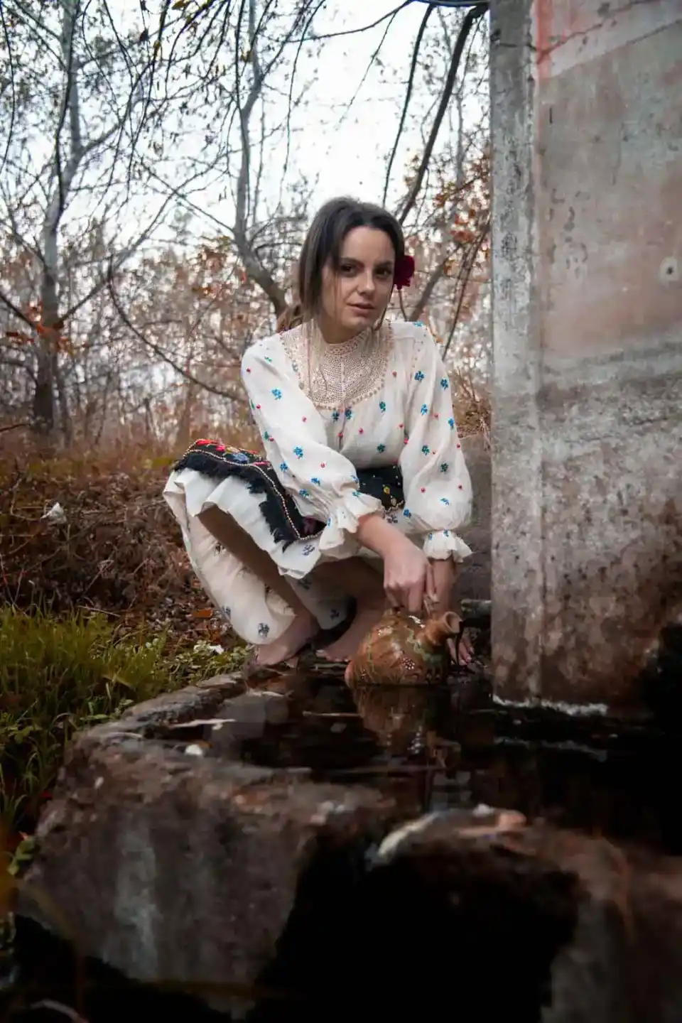 Junge Frau in traditioneller Tracht sitzt an einem Waldbach, Portrait Wien von Fotograf Alexandru Bogdan