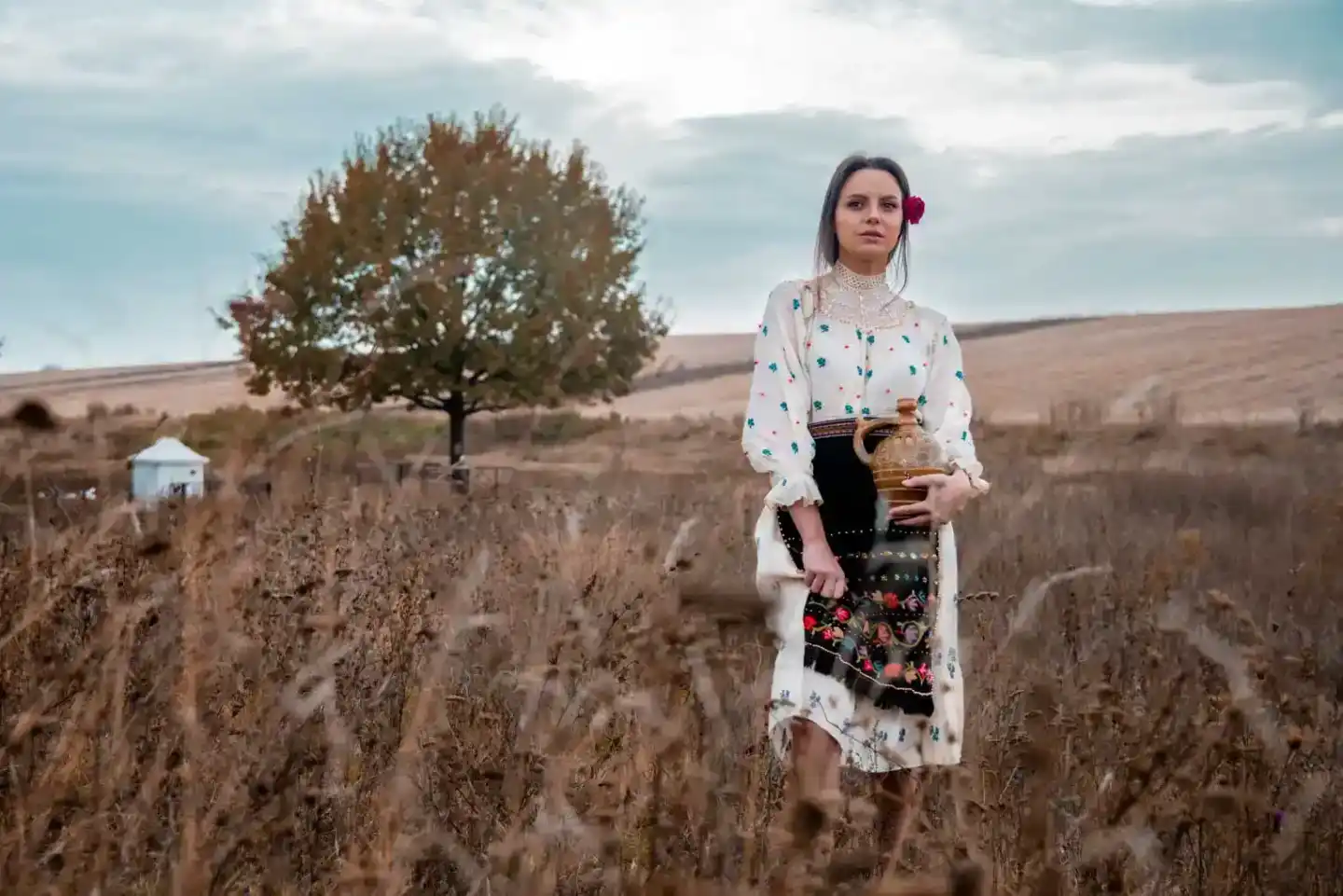 Junge Frau in traditioneller ukrainischer Tracht mit weißer bestickter Bluse hält einen Krug in einem herbstlichen Feld – pro
