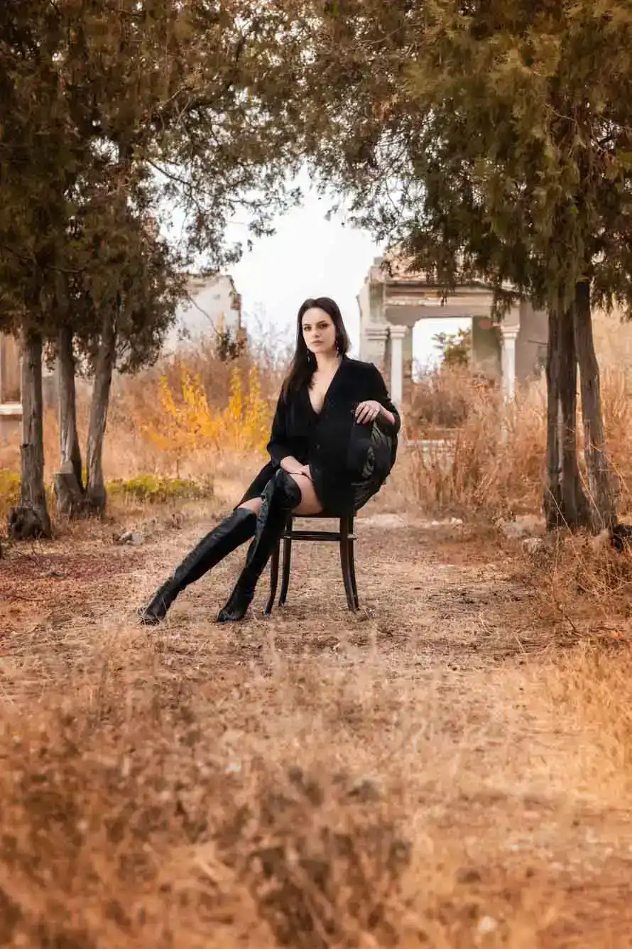 Elegantes Portraitfoto einer Frau in schwarzem Blazer, sitzend auf Stuhl unter Bäumen in Wien