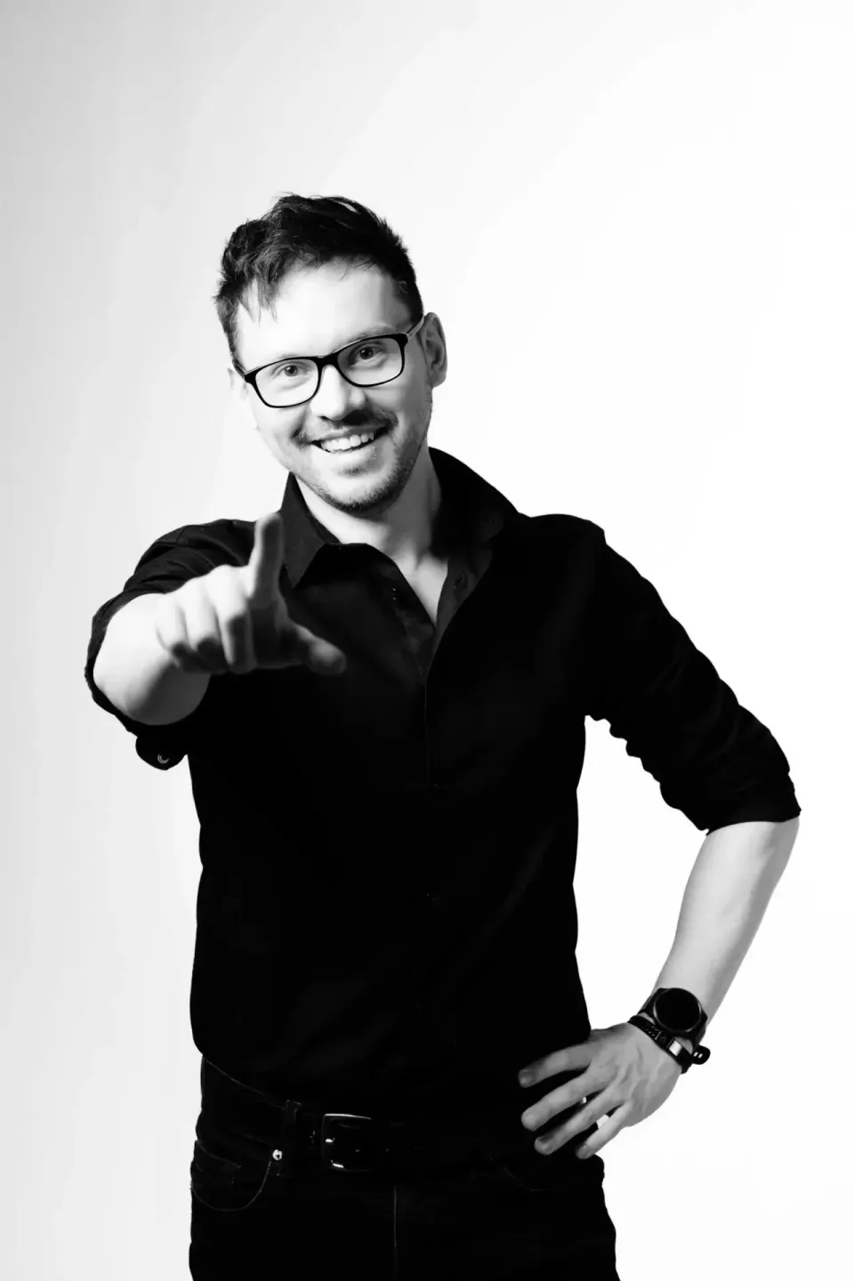 Porträtfoto eines lächelnden Mannes mit Brille in schwarzem Hemd, der in die Kamera zeigt - professionelles Portrait Wien