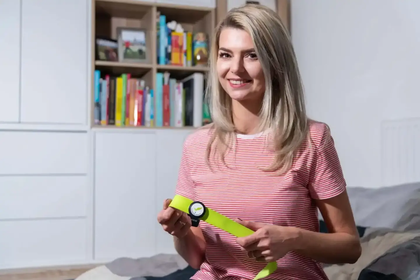 Junge Frau präsentiert Smartwatch mit neongelben Armband in modernem Wohnzimmer – Produktfotografie Wien