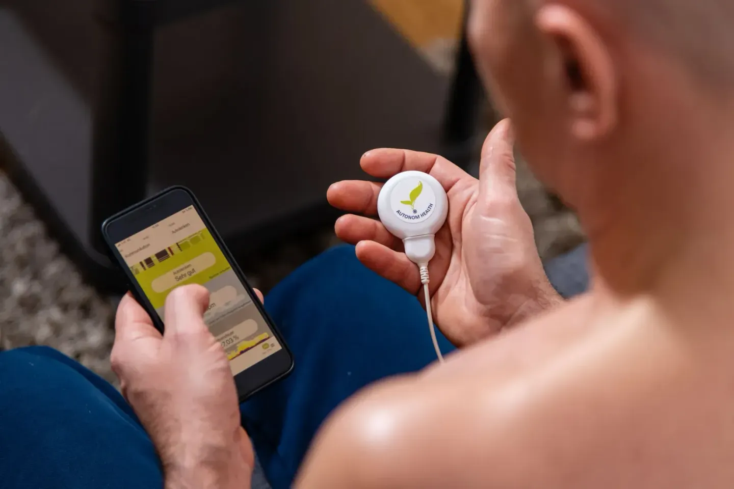 Mann hält weißes Smart-Home-Gerät in der Hand und schaut auf sein Smartphone – Produktfotografie Wien