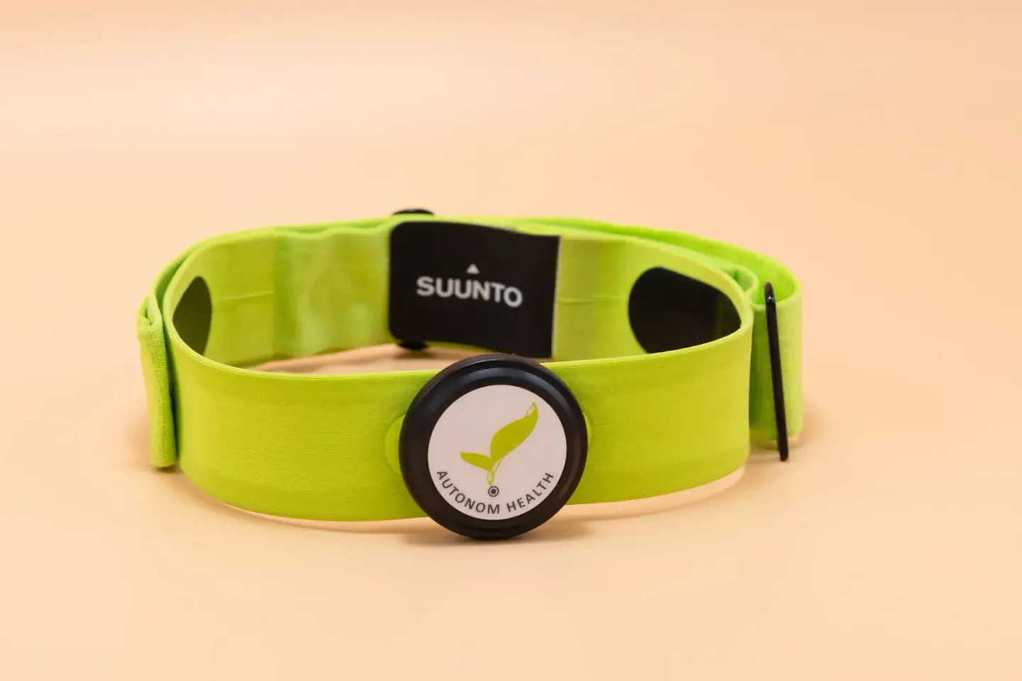 Grünes Suunto Sportarmband mit schwarzem Display und Autonomh Health Logo auf beigem Hintergrund - Produktfotografie Wien