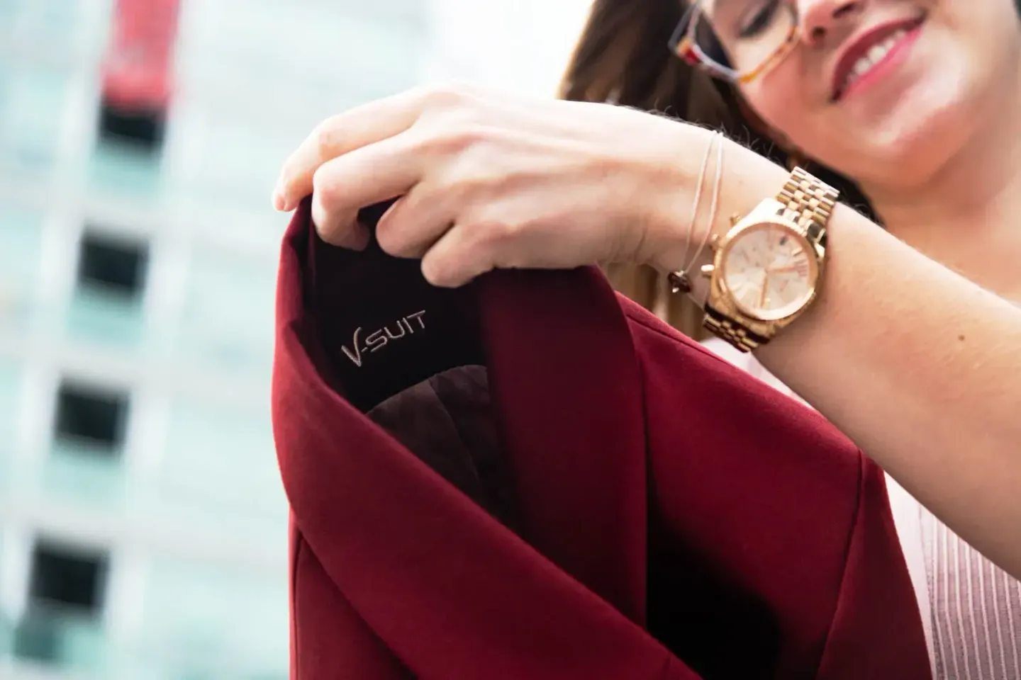 Frau in bordeauxrotem Blazer mit goldener Armbanduhr hält rote Visitenkartenhülle, Produktfotografie Wien