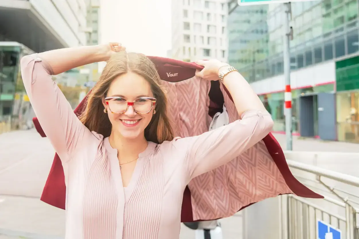 Junge Frau mit Brille präsentiert eine burgundrote Jacke auf einer Wiener Straße – Produktfotografie Wien