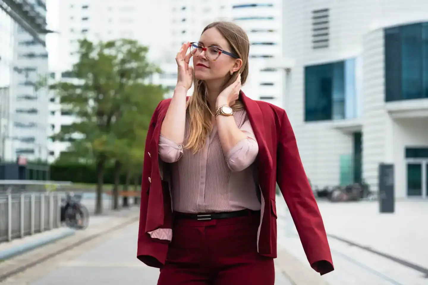 Geschäftsfrau in Bordeaux-Anzug und Brille vor modernem Bürogebäude in Wien – Produktfotografie für Geschäftsportraits