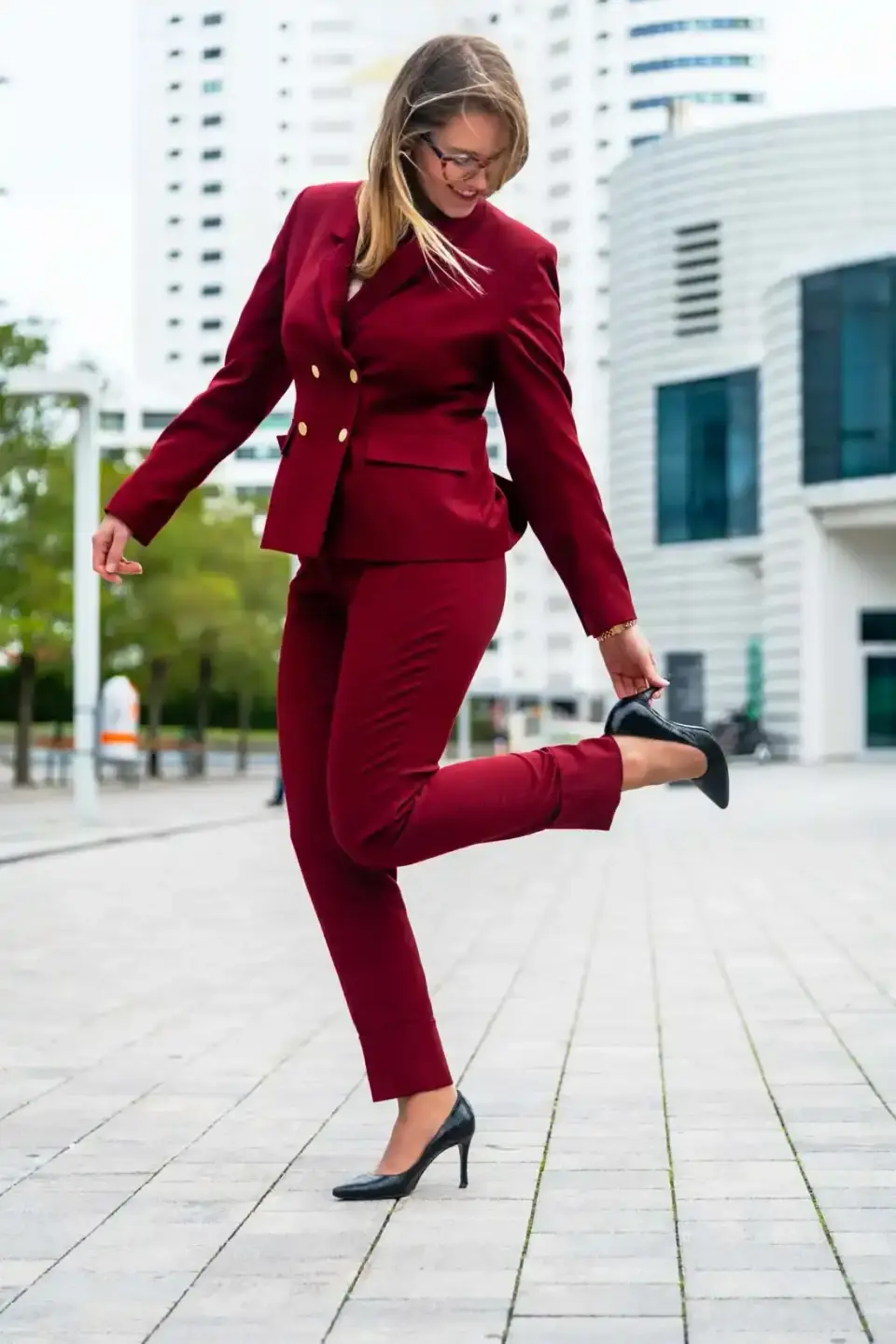 Frau in burgunderfarbenem Businessanzug springt vor modernen Hochhäusern in Wien - Produktfotografie für Corporate-Styling