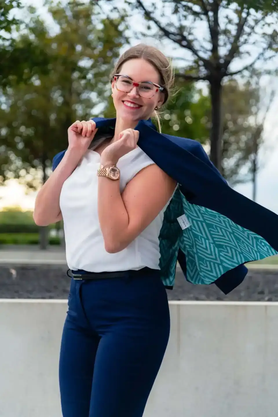 Junge Frau in Business-Outfit mit weißem Top, blauer Blazer und Uhr posiert selbstbewusst im Park – Werbefotografie Wien