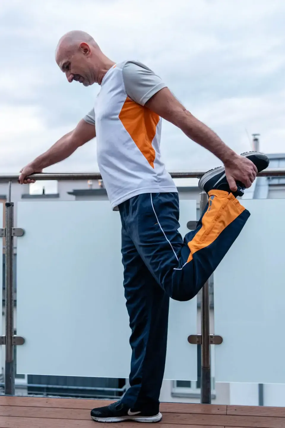 Mann in Sportkleidung mit Orange-Details dehnt sein Bein auf einer Terrasse - Produktfotografie Wien