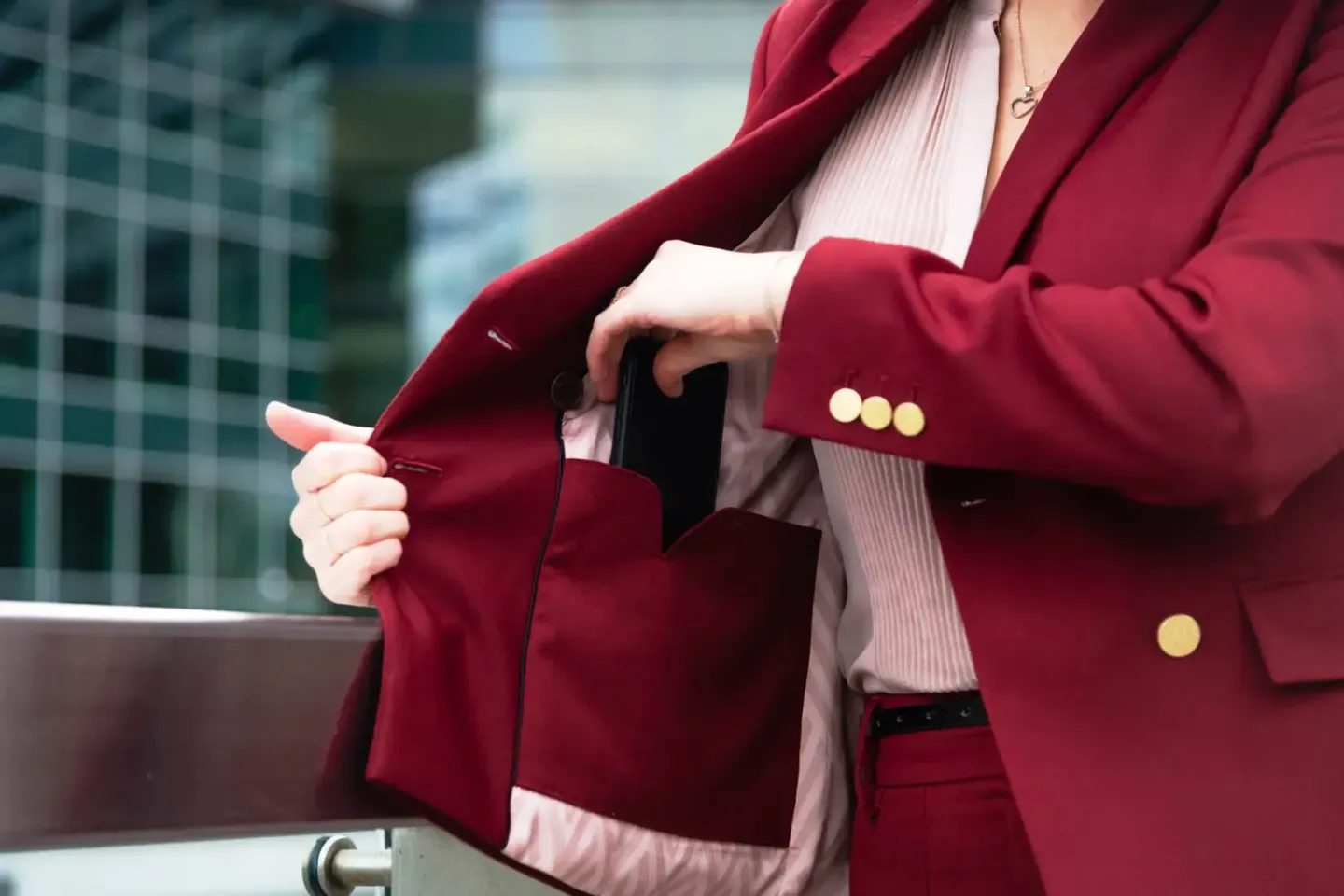 Geschäftsfrau in burgunderrotem Blazer mit goldenen Knöpfen hält schwarzes Smartphone in der Hand - Produktfotografie Wien