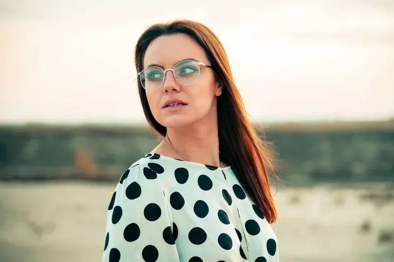 Junge Frau mit Brille und rötlichen Haaren trägt gepunktetes Shirt an Wasserkante, Produktfotografie Wien