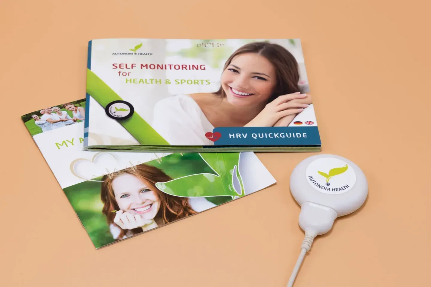 Produktfotografie Wien: Aunom Health Self Monitoring Set mit Quickguide, Sensor und Verpackung auf beigem Hintergrund
