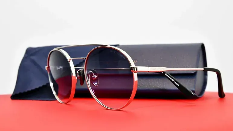 Hochwertige Sonnenbrille mit rotem Metallrahmen und dunklen Gläsern neben Etui – Produktfotografie Wien