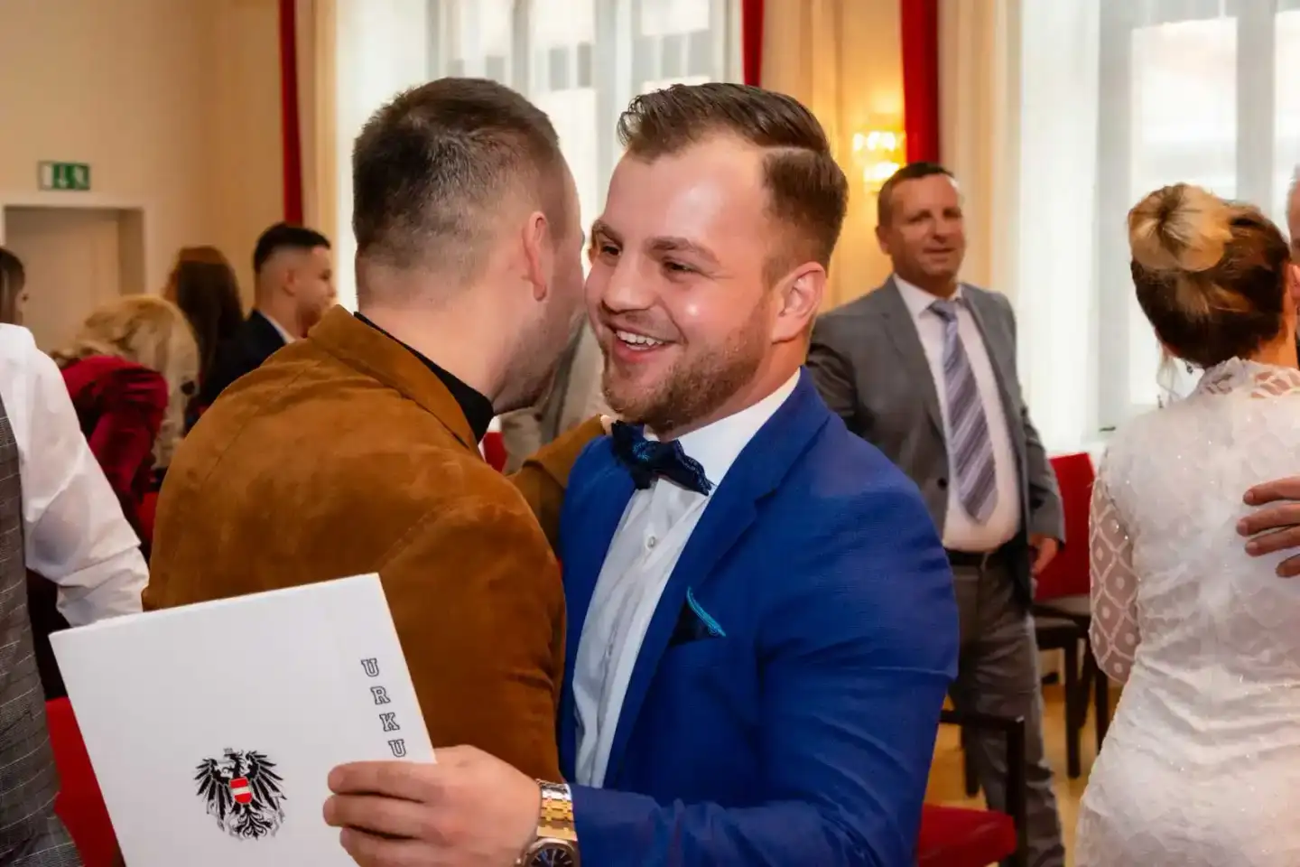 Bräutigam in blauem Anzug gratuliert Gast bei Hochzeitsfeier Wien, beide lachen herzlich