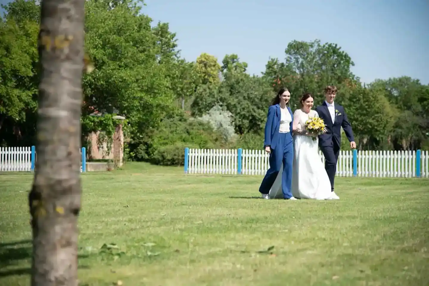 Brautpaar mit Trauzeugin im grünen Park bei Hochzeitsfotografie Wien, Braut trägt gelben Blumenstrauß