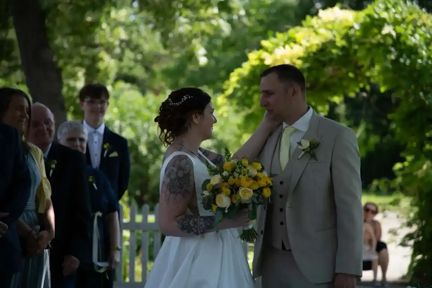 Brautpaar steht sich gegenüber während der Trauung im grünen Park, Hochzeitsfotografie Wien mit Gästen im Hintergrund