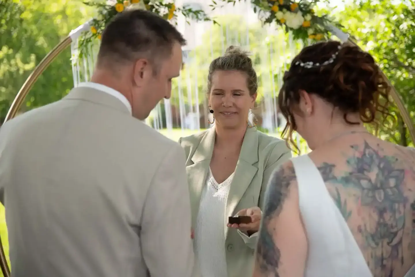 Standesbeamtin traut Brautpaar unter blumiger Laube bei Hochzeitsfotografie Wien