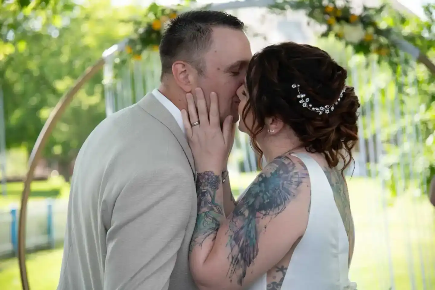 Brautpaar küsst sich unter Blumenbogen im Garten – professionelle Hochzeitsfotografie Wien