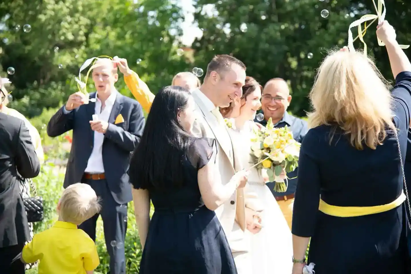 Brautpaar wird von Hochzeitsgästen mit gelben Schleifen und Seifenblasen begrüßt, Hochzeitsfotograf Wien dokumentiert den Mom