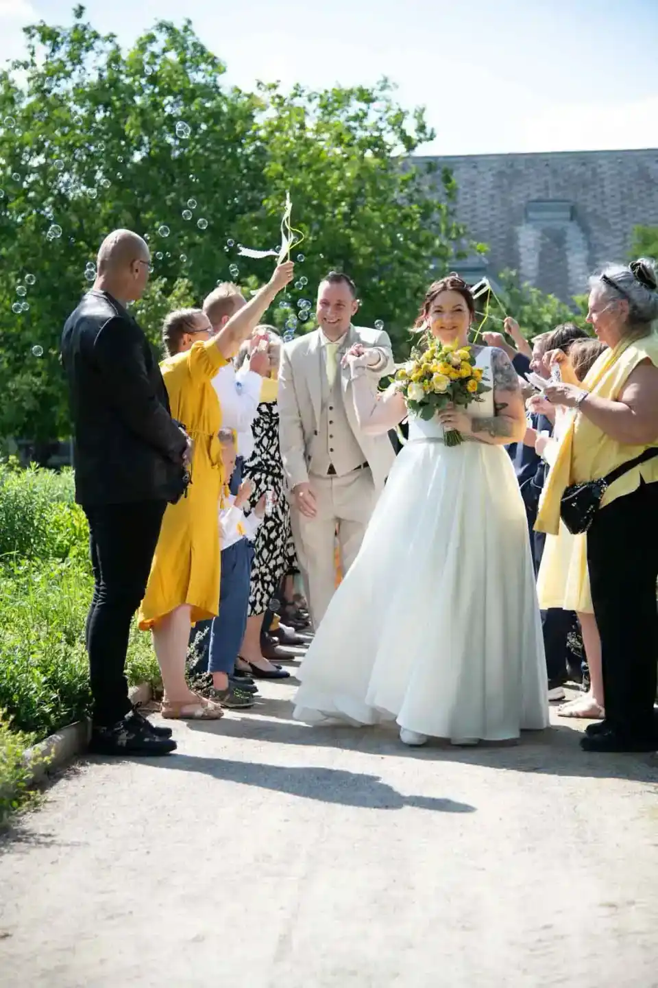 Brautpaar bei Seifenblasen-Exit, umringt von Hochzeitsgästen in gelben Outfits, professionelle Hochzeitsfotografie Wien