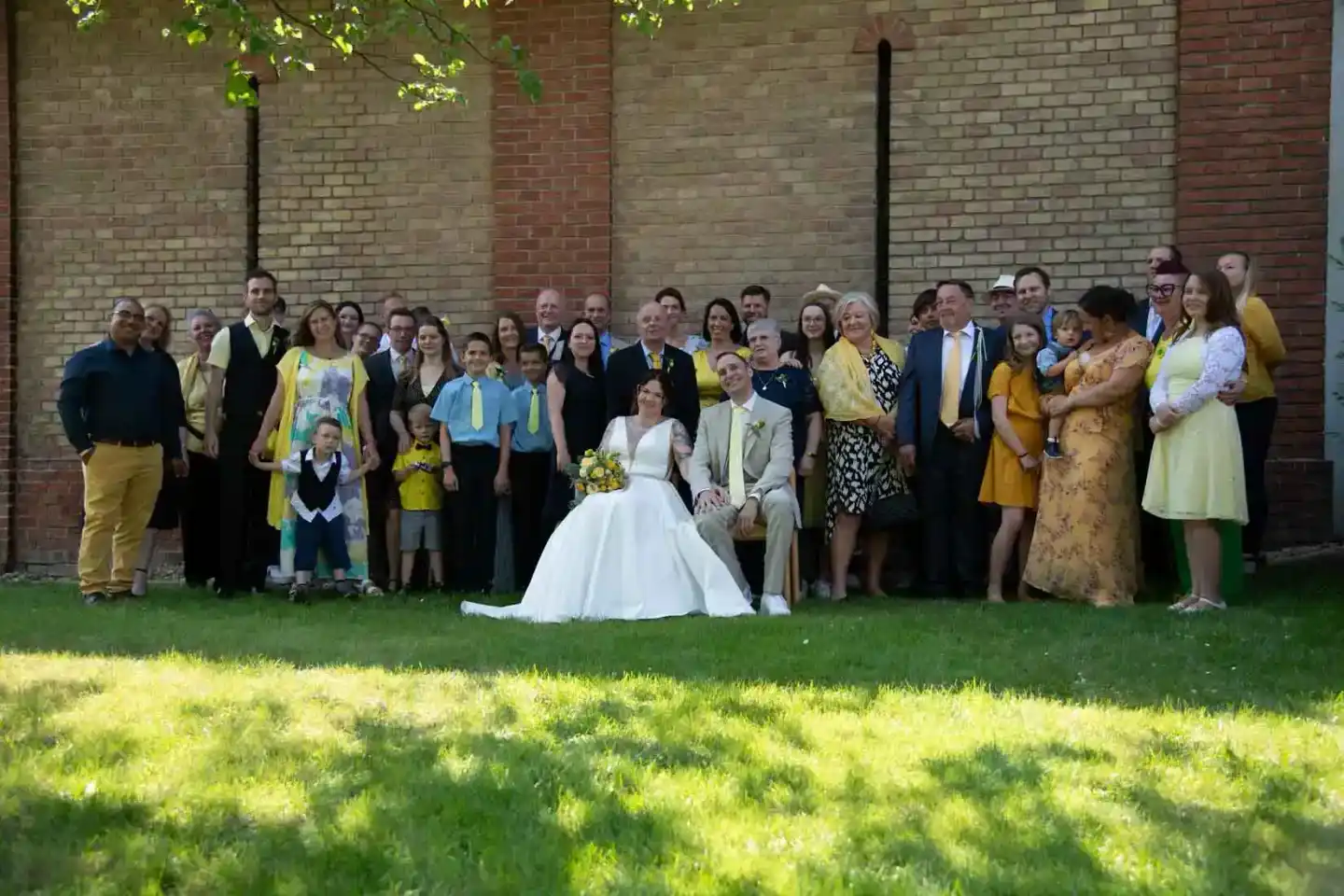 Brautpaar sitzt auf einer Bank vor einer Hochzeitsgesellschaft in einem Garten, professionelle Hochzeitsfotografie Wien