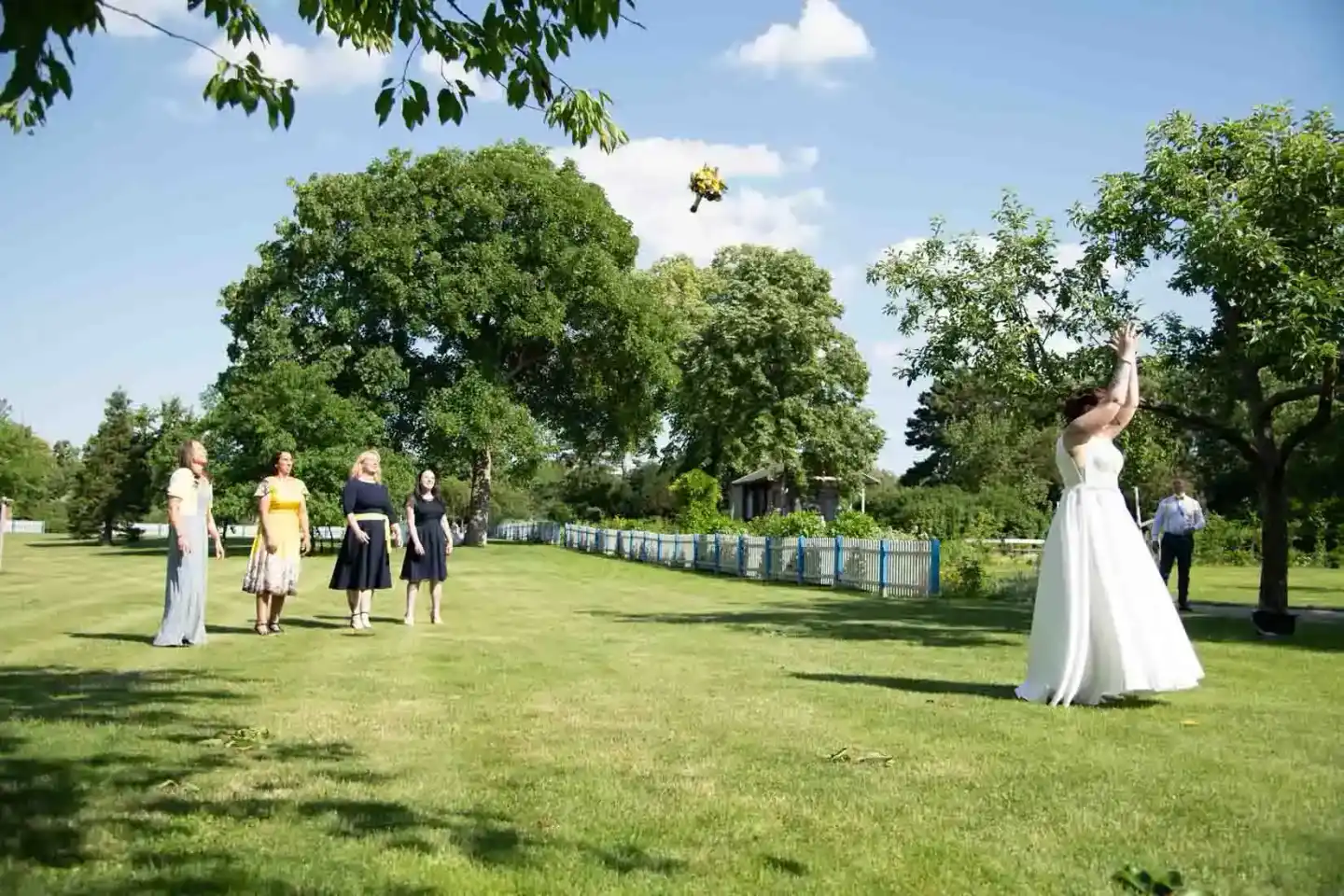 Braut in weißem Kleid wirft Brautstrauß beim Hochzeitsfest im Freien, umgeben von Hochzeitsgästen - Hochzeitsfotografie Wien