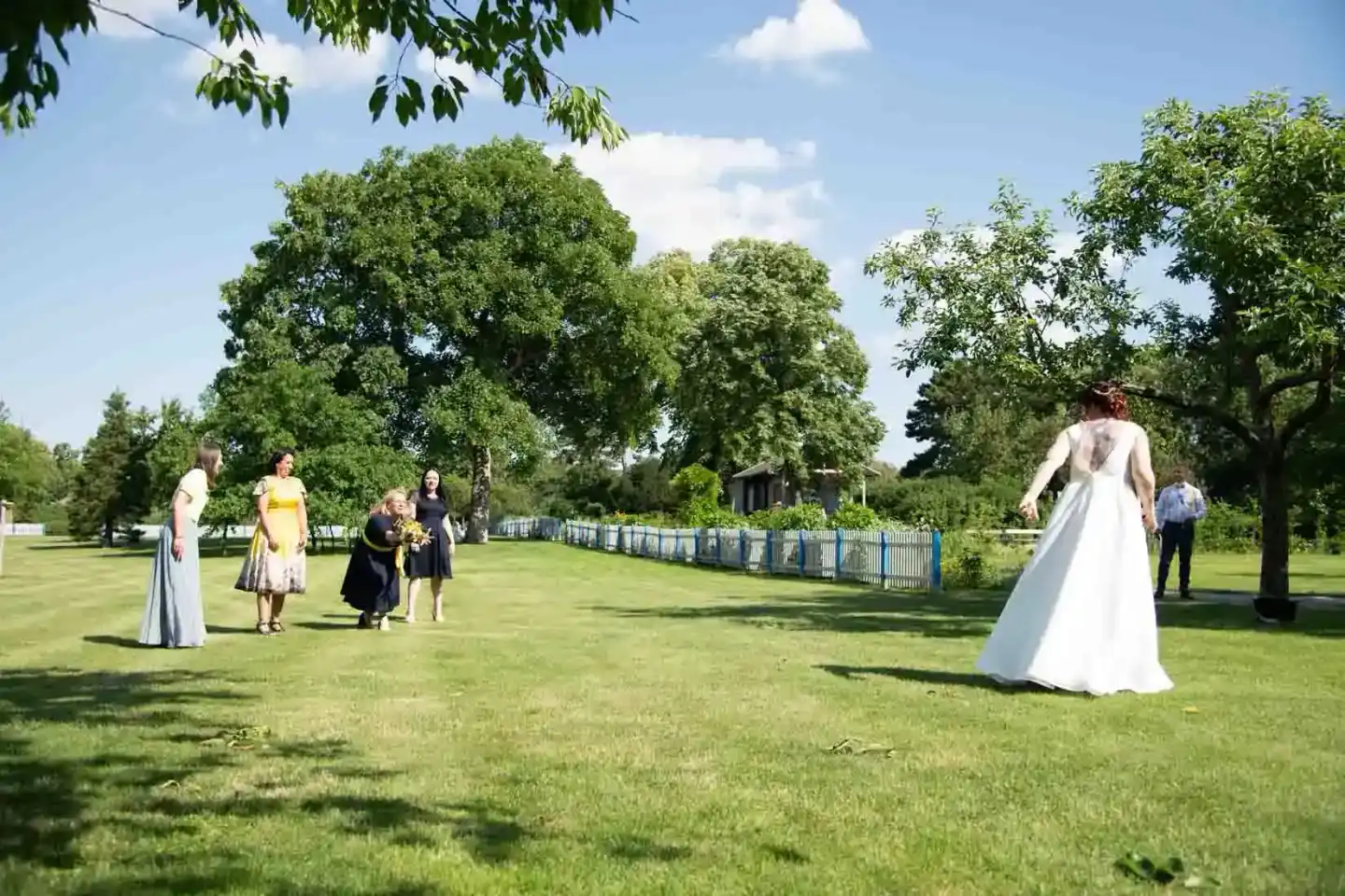 Braut in weißem Hochzeitskleid auf grüner Wiese mit Gästen, Hochzeitsfotograf dokumentiert Moment im Park