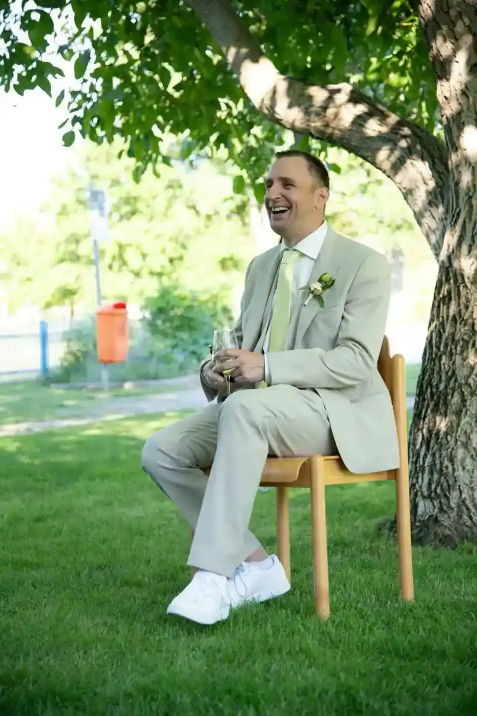 Glücklicher Bräutigam sitzt unter einem Baum bei einer Hochzeit in Wien und hält ein Champagnerglas