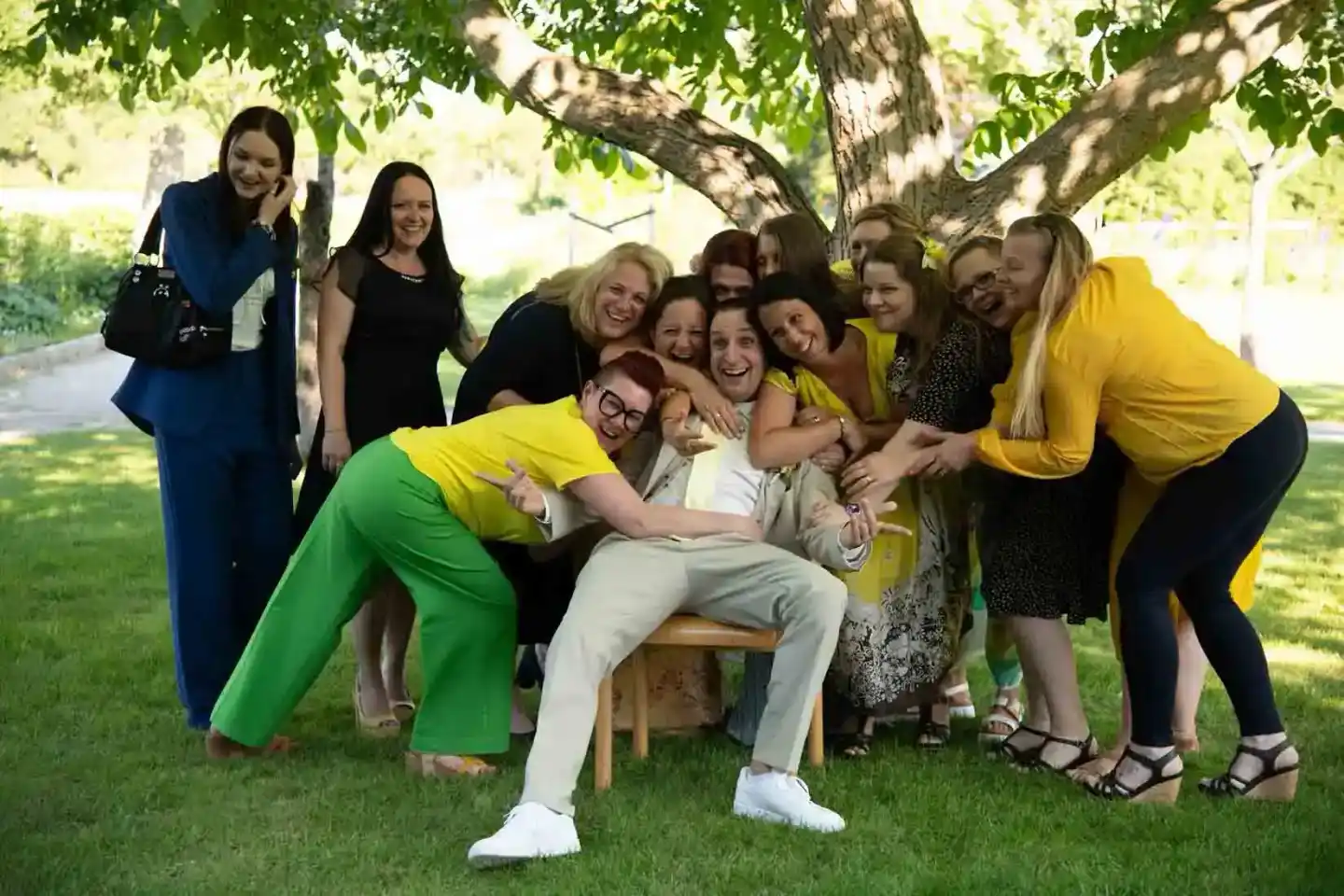 Brautjungfern und Freunde umarmen strahlend die Braut unter einem großen Baum – Hochzeitsfotografie Wien