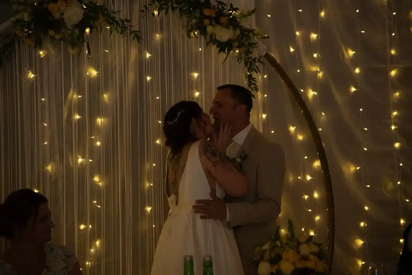 Brautpaar küsst sich vor glänzender LED-Lichterwand mit Blumendekoration – Hochzeitsfotografie Wien