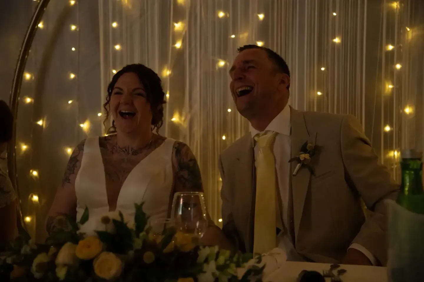 Brautpaar lacht glücklich beim Hochzeitsessen vor einer beleuchteten Gardine – Hochzeitsfotografie Wien