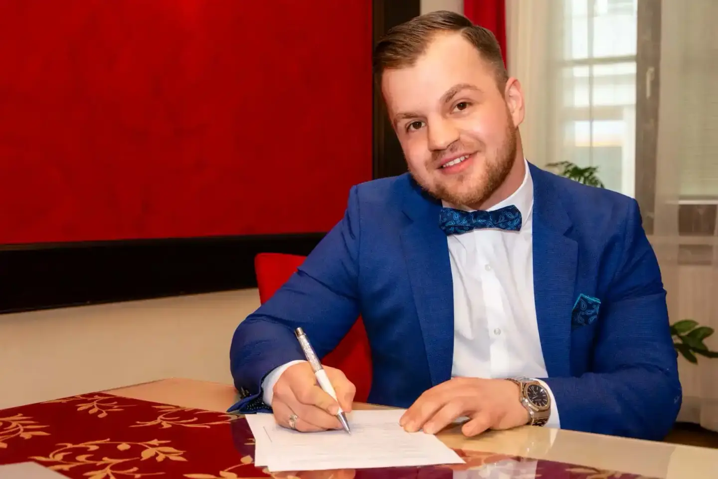 Eleganter Mann im blauen Anzug mit Fliege unterzeichnet Hochzeitsdokumente – professionelle Hochzeitsfotografie Wien