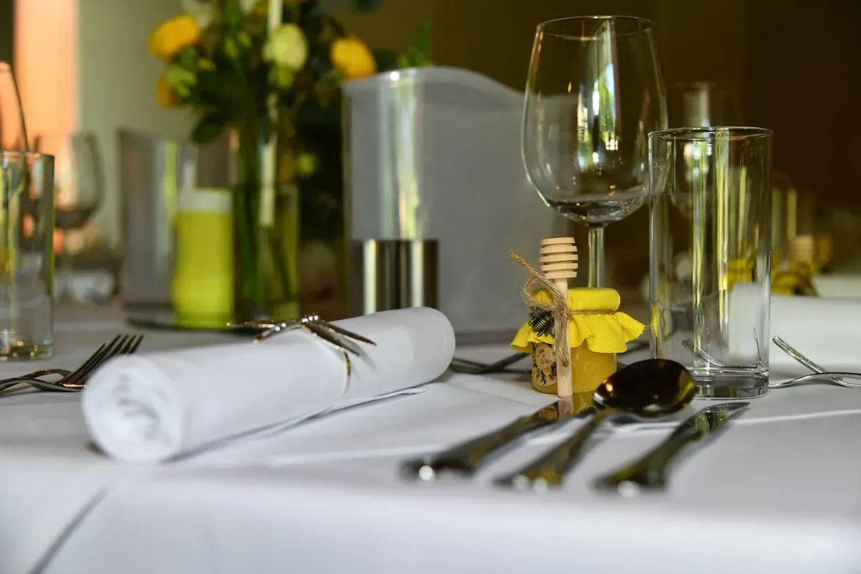Elegant gedeckter Hochzeitstisch mit weißer Serviette, Besteck, Gläsern und gelben Blumen als Tischdekoration für eine Hochze